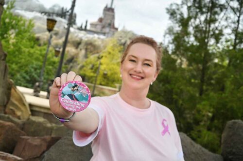 DeAnna wearing a pink ribbon shirt holding a pin celebrating finishing cancer treatment