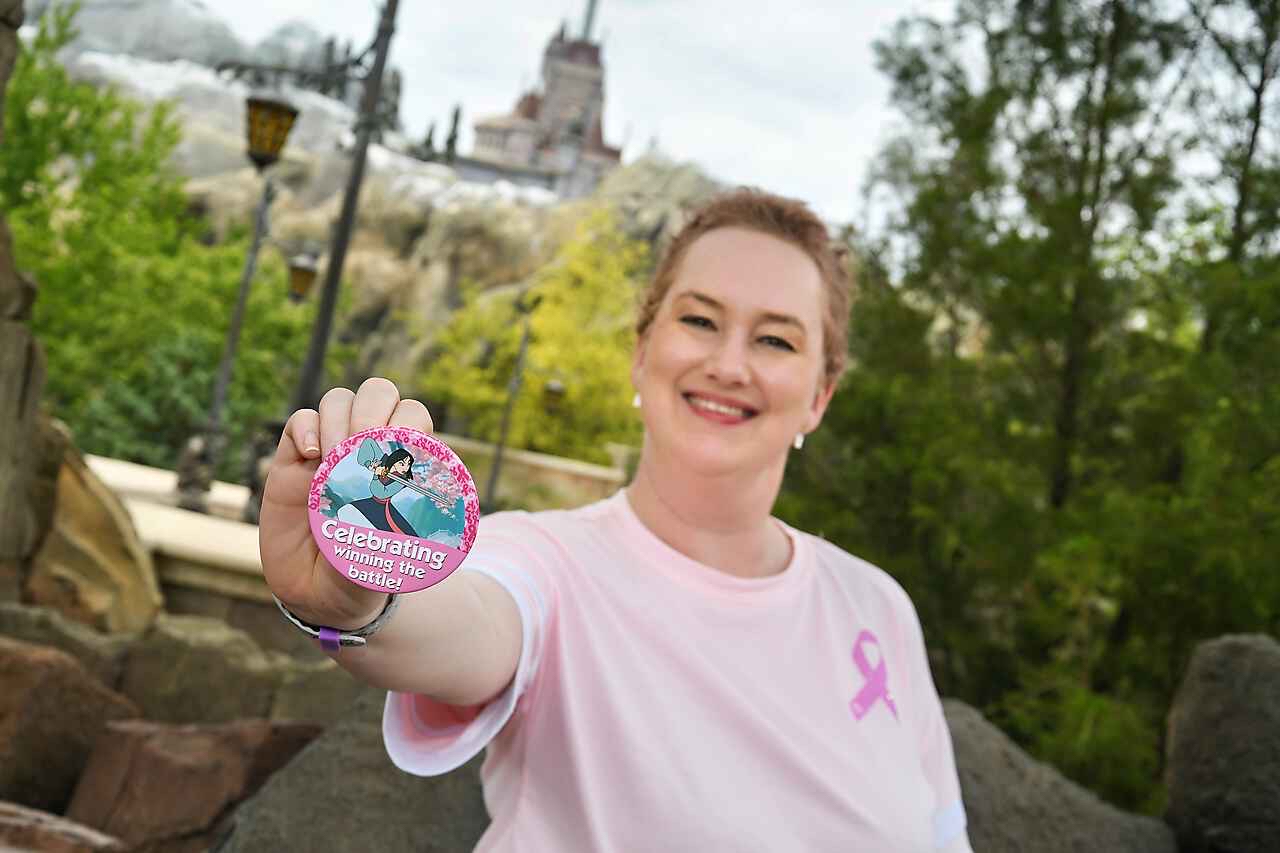 DeAnna wearing a pink ribbon shirt holding a pin celebrating finishing cancer treatment